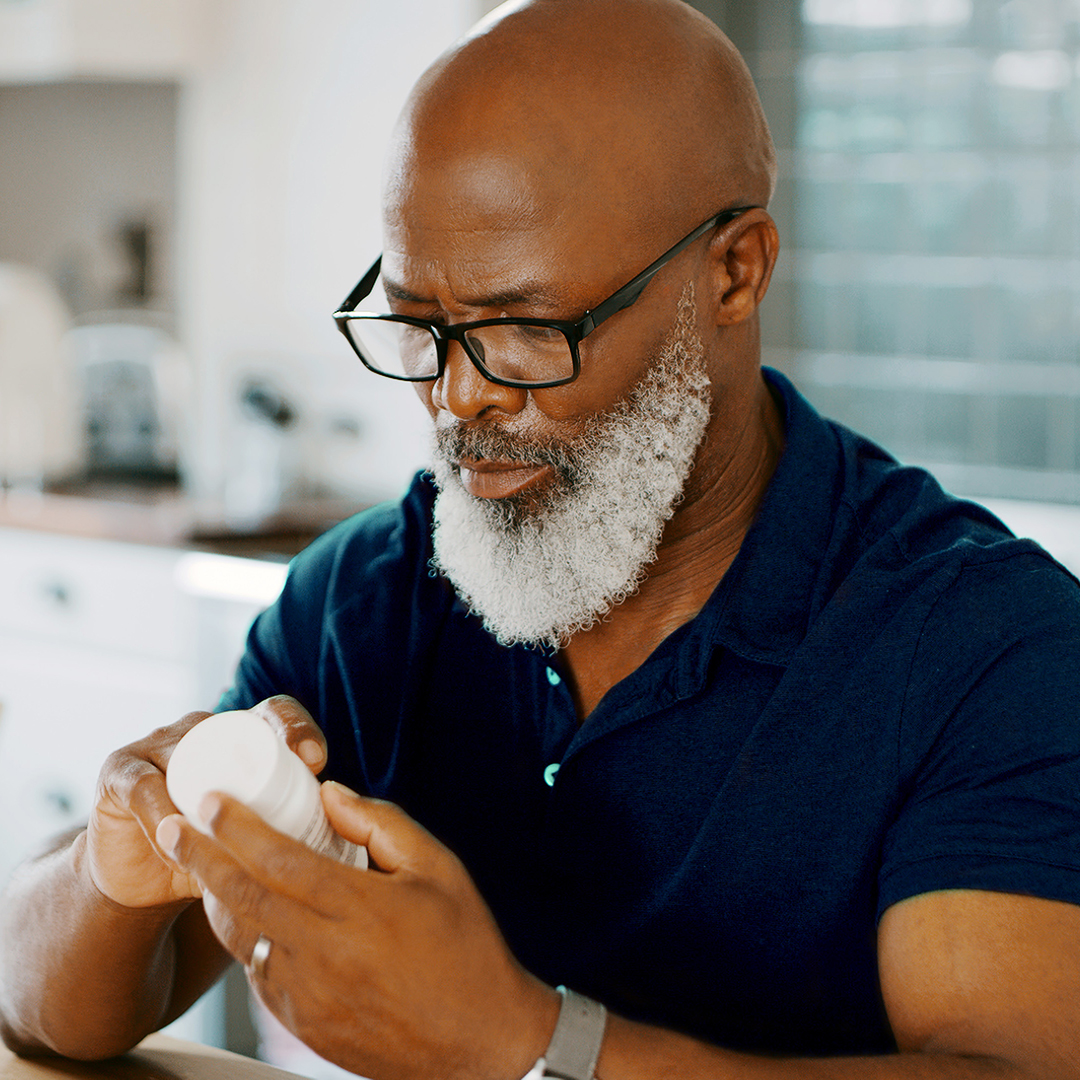 A man reads a medication label at his kitchen table.