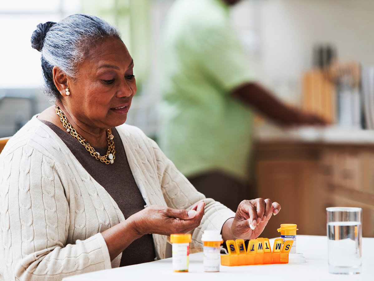 An older woman sorts her medication doses into a weekly pill organizer.