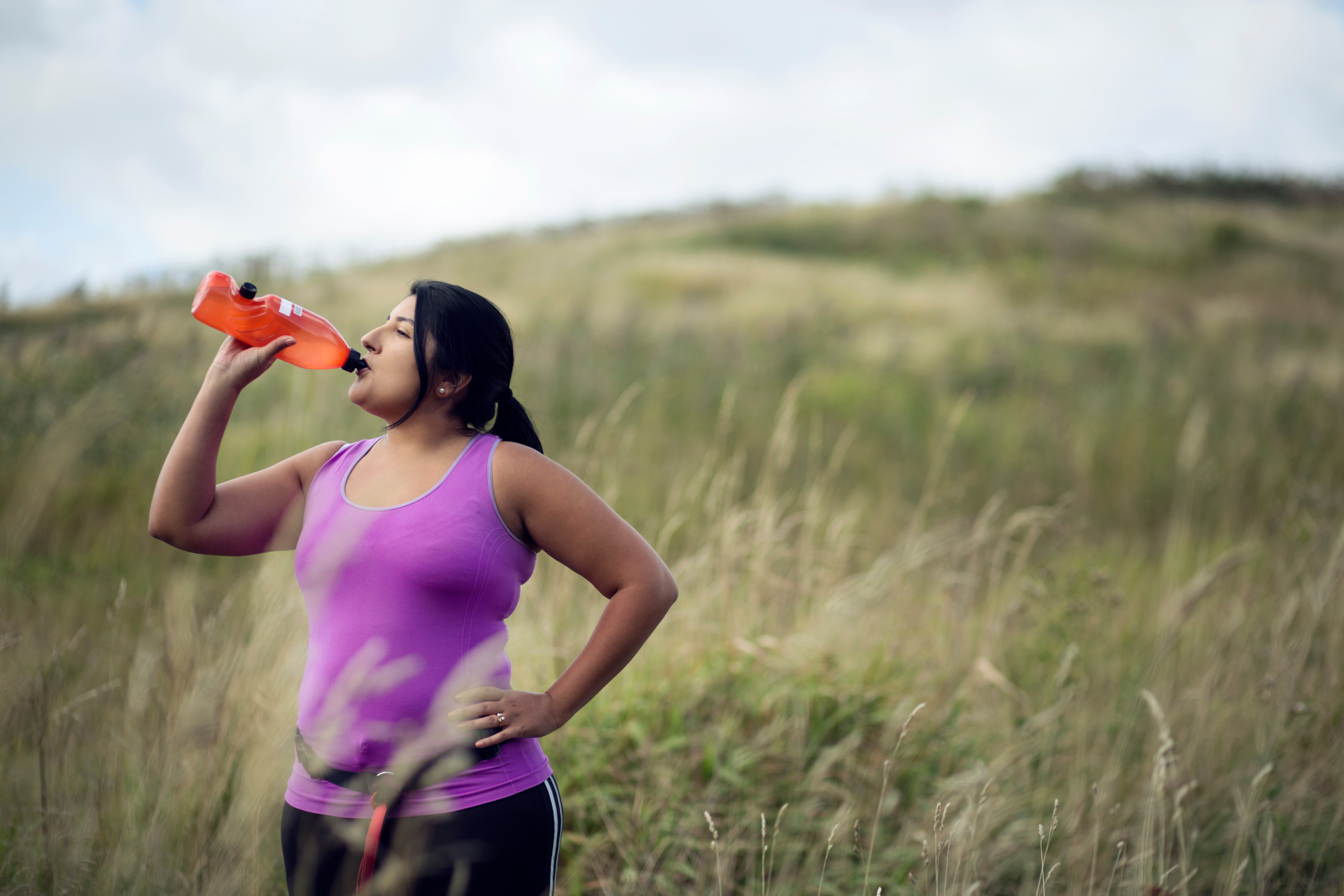 A woman in a field drinks from a water bottle