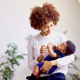 A young mom holds her baby in her arms while smiling at him.