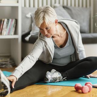 An older woman stretches on a mat on the floor of her home.